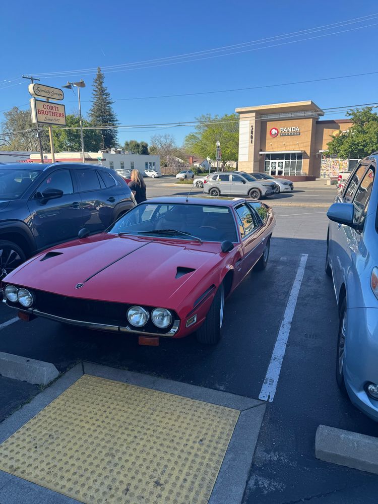 A red Lamborghini Espada parked at a neighborhood grocery store.
