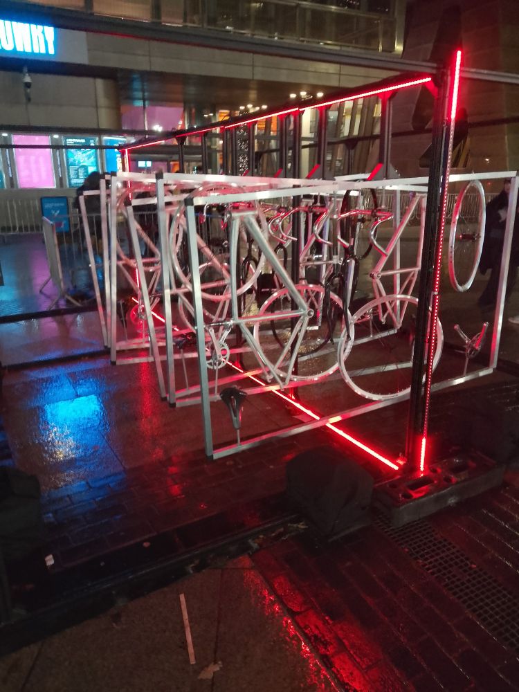 A series of bicycles hanging in frames, illuminated by lights surrounding it.