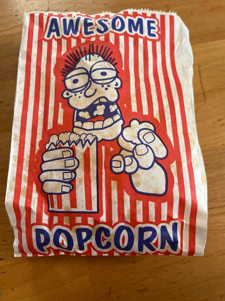 A red and white stripes popcorn bag with a goofy ass looking cartoon dude shoveling into his toothy grin.