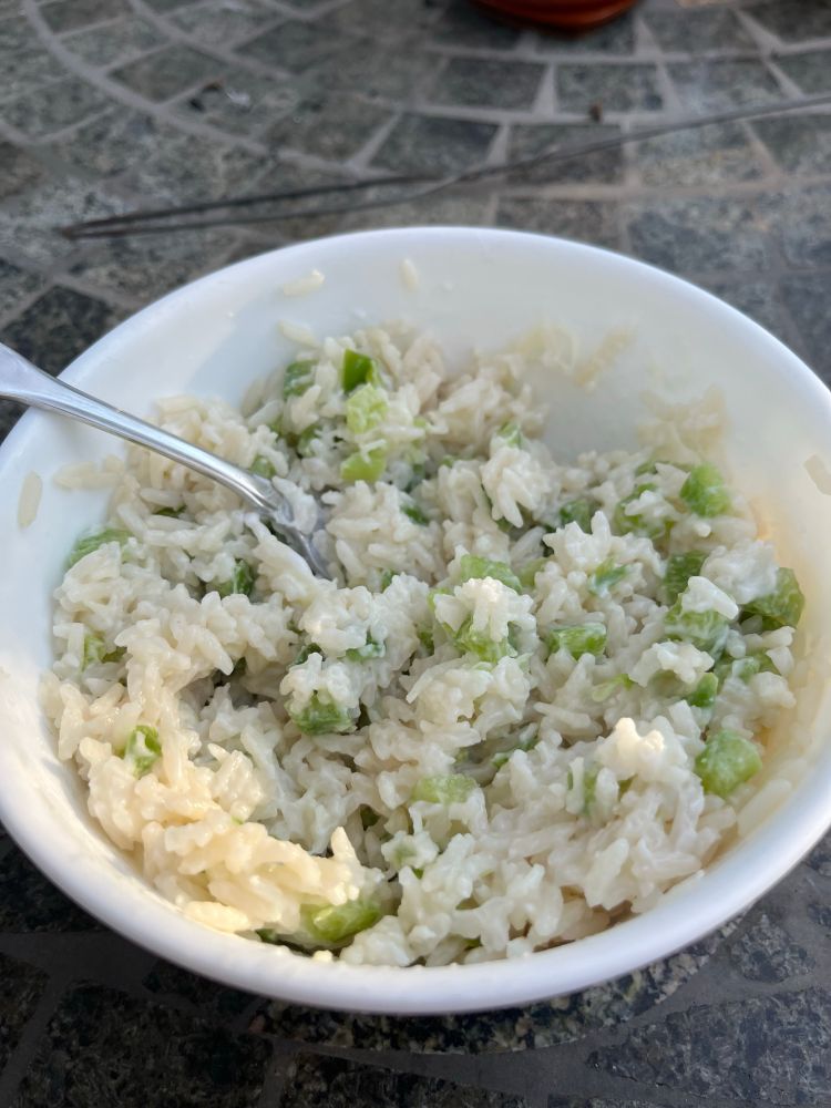 A picture of a bowl of rice with diced green peppers, cream cheese, and cheese all mixed together. There is a silver fork sticking into it. 