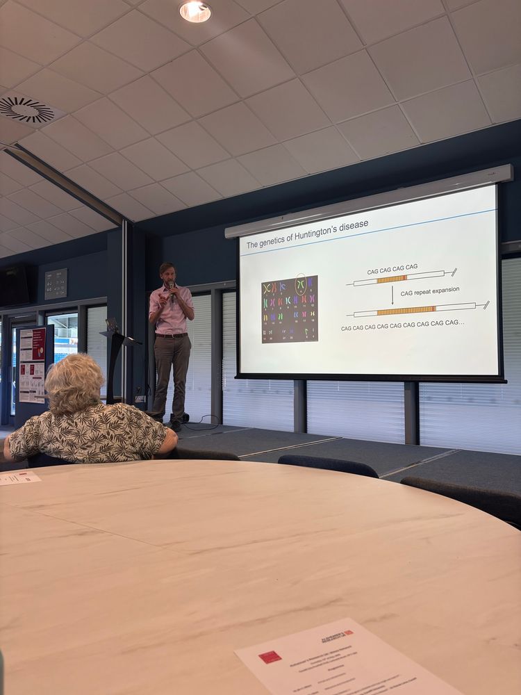 Image shows a researcher in a stage explaining Huntington’s disease. He is talking about the CAG expansion found in this disease. 