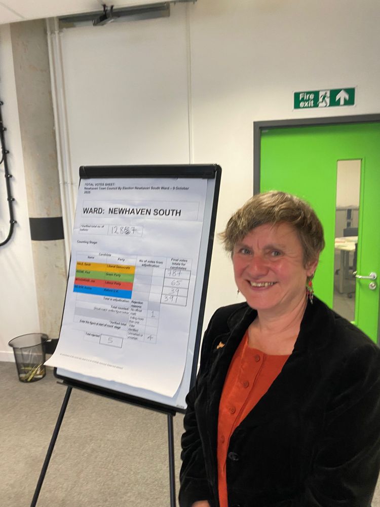 Sarah Hale, looking delighted stands next to a flipboard showing the votes: LibDem 787, Greens 65, Labour 39, Reform 391.