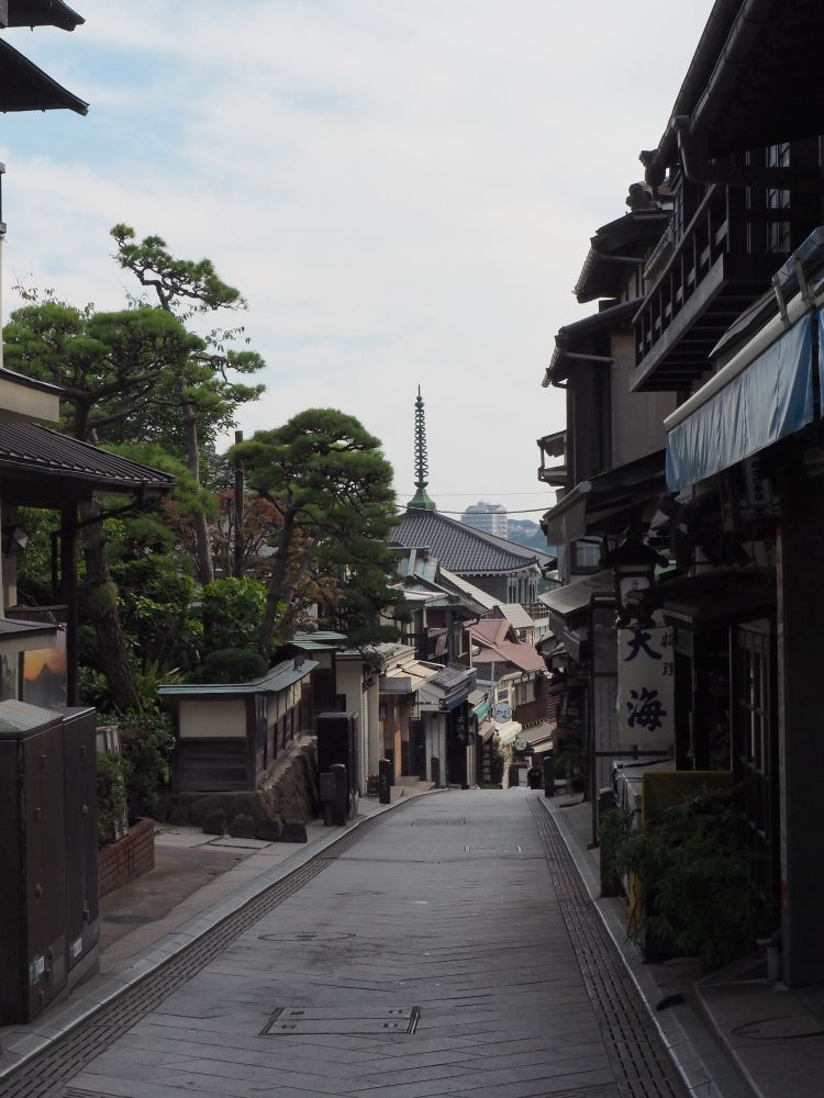 Man sieht eine schmale Straße in Japan. Rechts und links stehen alte Häuser. Im Hintergrund sieht man die Spitze einer Pagode. Die Straße ist lehr, da es noch sehr früh am Morgen ist.