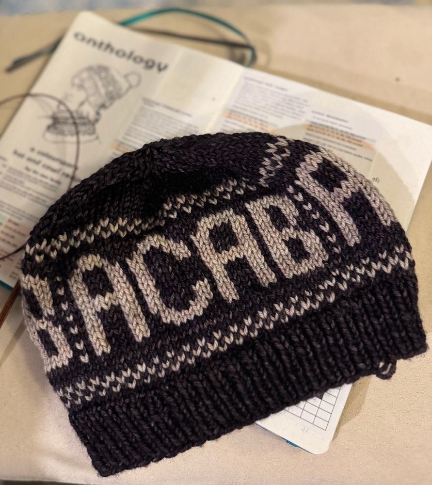 Dark brown hat with big tan lettering that says “ACAB” with some decorative edging. It’s laying on top of a notebook with the pattern in it. 