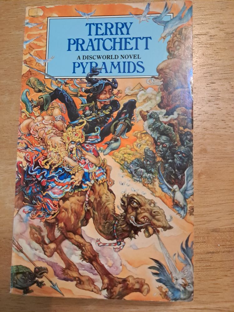 The cover of Pyramids by Terry Pratchett. This is the Corgi paperback edition with the Josh Kirby cover showing Teppic and Ptraci on a camel.