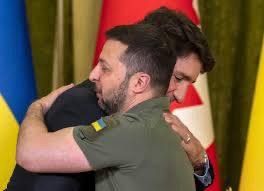 Volodymyr Zelenskyy and Justin Trudeau embrace each other in this photo. Flags of Ukraine and Canada are in background.