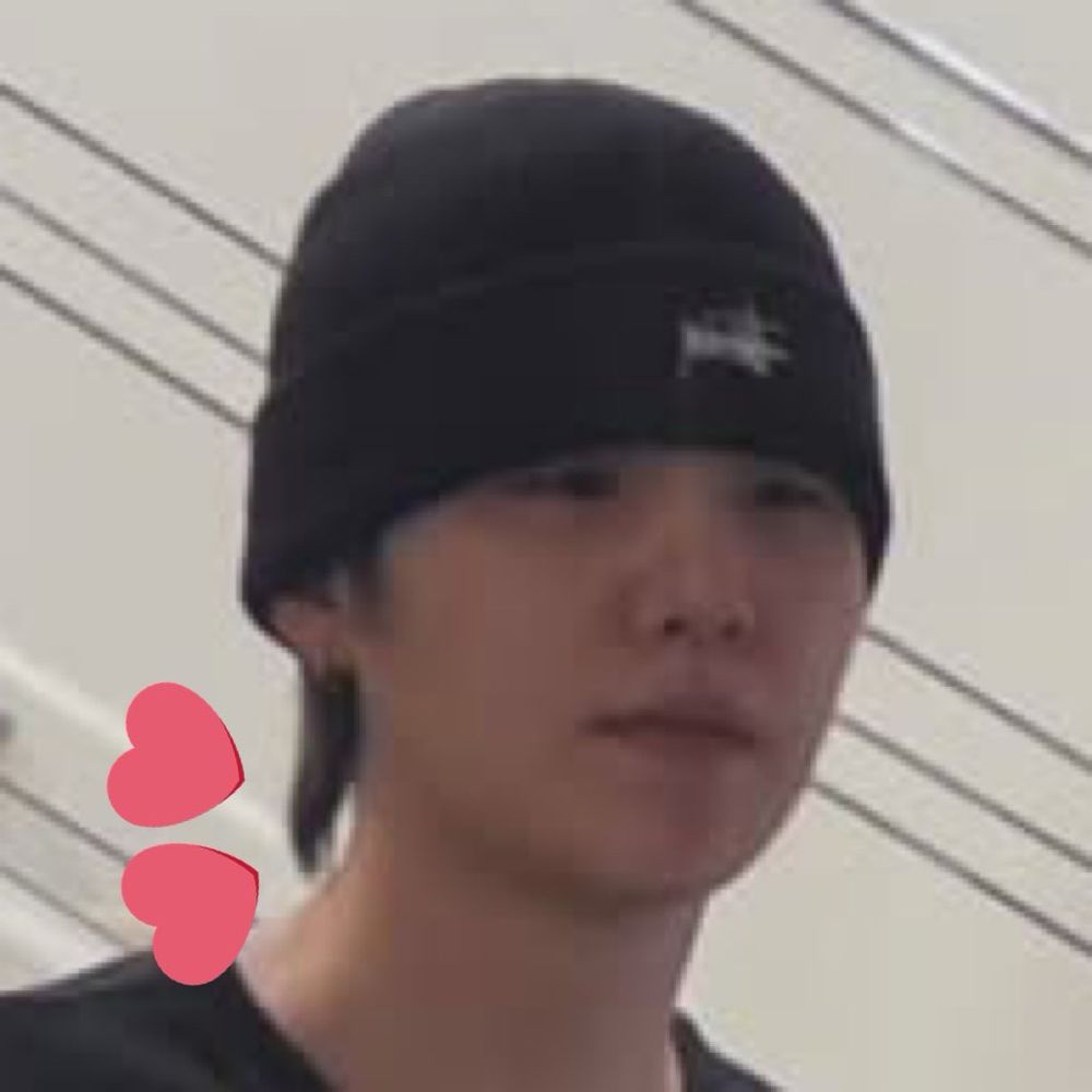 Close up of yoongi’s face from a mirror selca of Hobi and Yoongi. Yoongi is in a black shirt and black beanie with a neutral expression on his face. Several inches of black hair are sticking out at the vape of his neck from the beanie 
