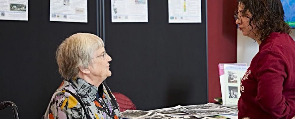 Dr Julia Neville is seated talking to a young woman about local history.