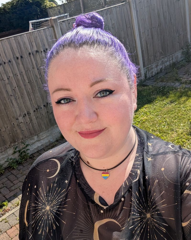 A photo of tabby with her hair in bun, wearing a black mesh top and a pan heart necklace