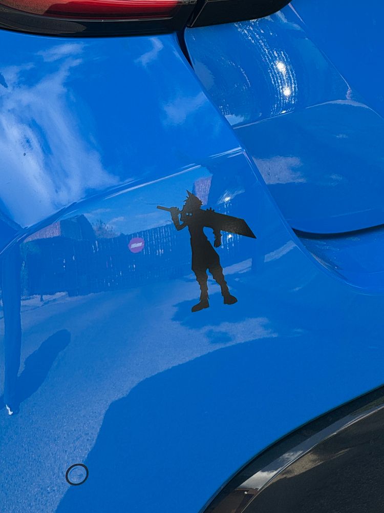 Close-up de la parte trasera de un coche color azul eléctrico. En el centro de la imagen se ve una pegatina de vinilo de color negro con la silueta del personaje Cloud Strife del videojuego Final Fantasy 7.