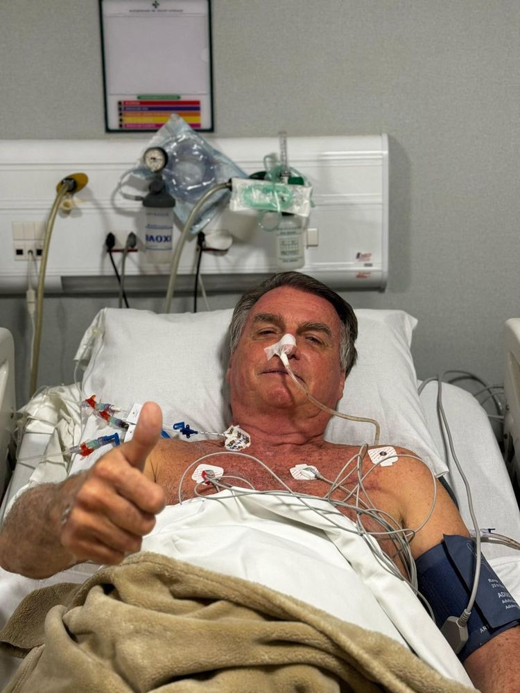 Bolsanaro giving the thumbs up in one of his many MANY hospital trips. 