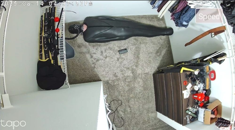 A sleepsacked and hooded gimp lying on the floor of the closet with a urinal and hose connected to the mouth of its hood.