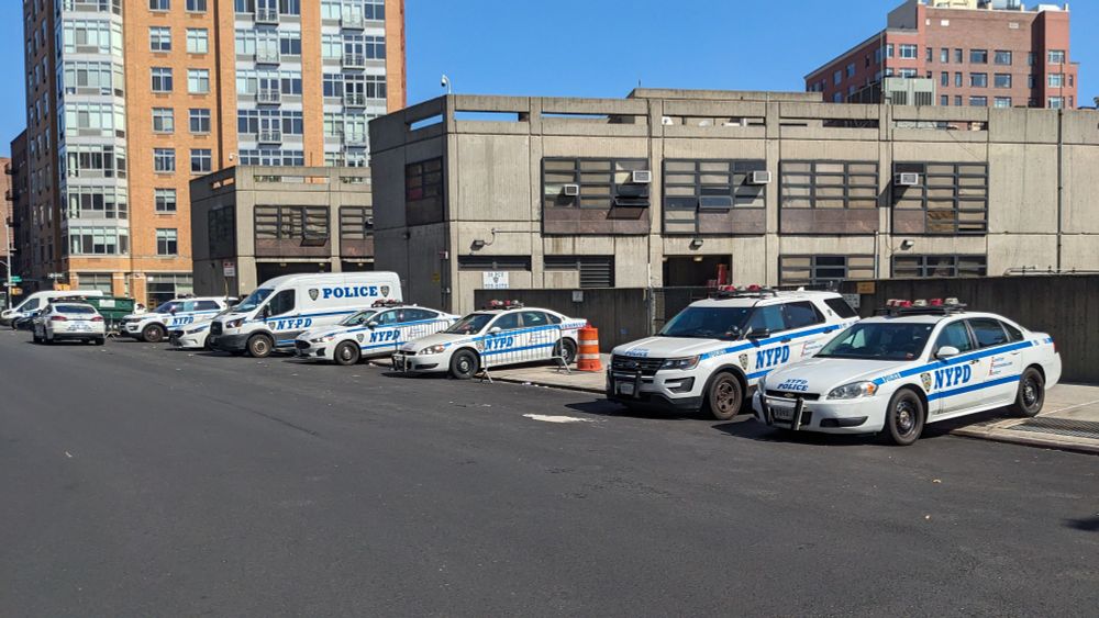 6 police cars parked half on the sidewalk with fronts sticking out on to the road in a city