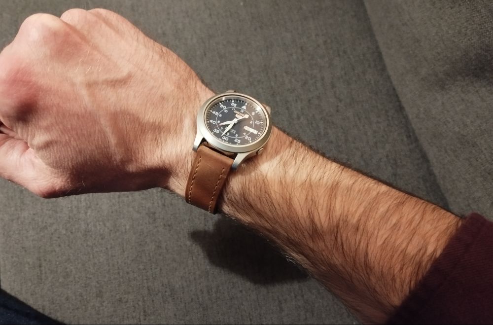 Montre automatique Seiko (ref SNK807 pour les nerds comme moi) à cadran militaire "flieger" bleu, portée à mon poignet droit. Ma manche est un peu remontée, on voit juste l'extrémité du poignet de ma chemise bordeaux 
