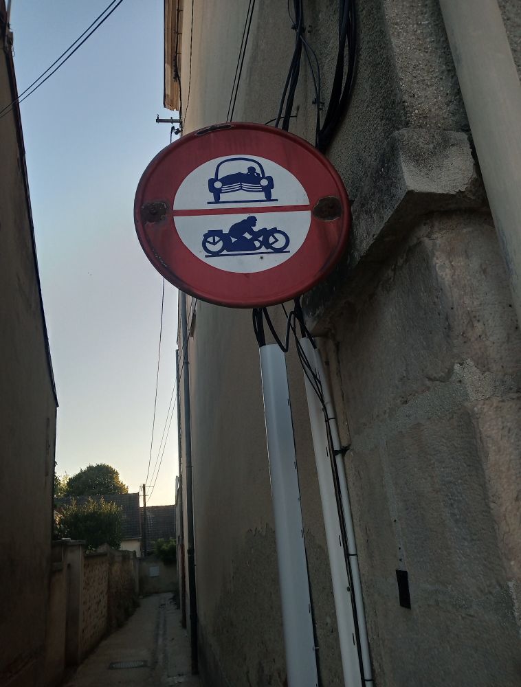 Vieux panneau de signalisation routière interdisant l'accès des voitures et motocyclettes dans une ruelle.