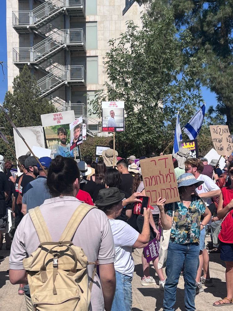 Protestierende in Jerusalem. Eine Frau hält ein Schild hoch, auf dem auf Hebräisch „Genug mit dem Krieg, genug mit dem Hungern“ steht. 