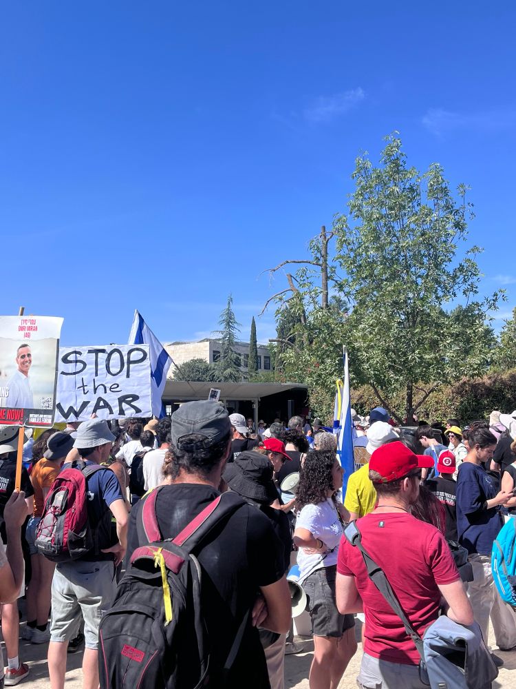 Protestierende in Jerusalem. Eine Person hält auf Englisch ein Schild mit „Stop the war“ hoch. 