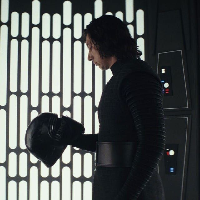Kylo Ren stands holding and looking at his helmet in a scene from The Last Jedi.