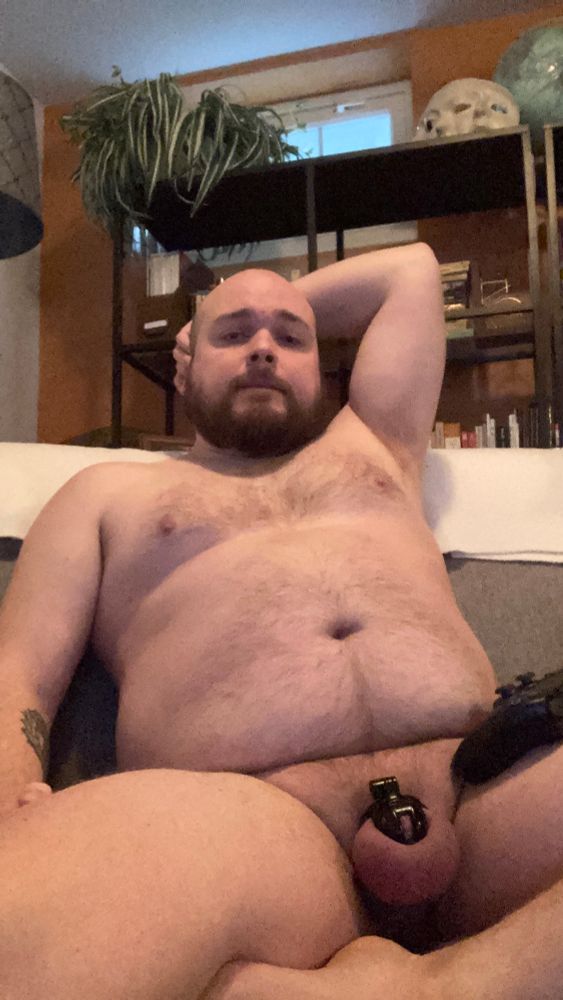 The artist, caged, with a PS5 controller on his thigh, relaxing on a couch. 