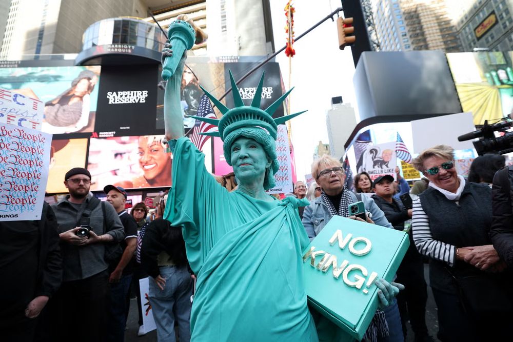 Lady dressed as the statue of liberty carrying a No King book.