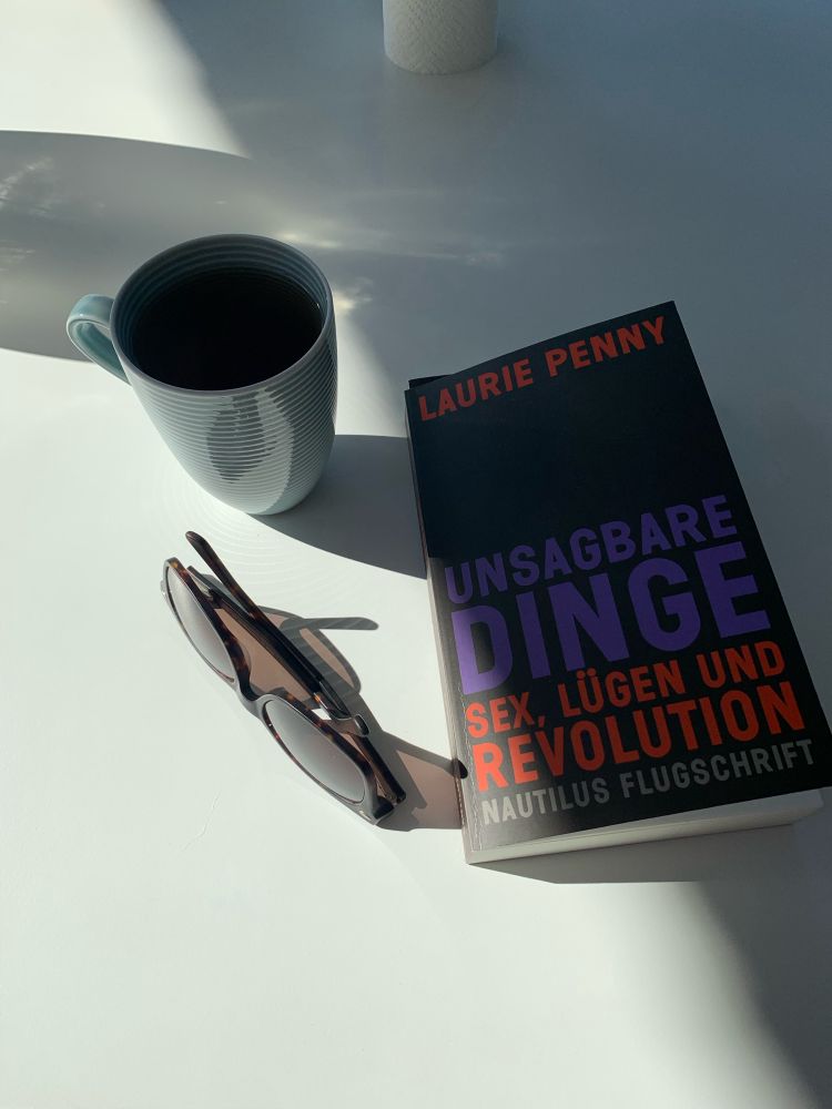 Eine Sonnenbrille, eine Tasse gefüllt mit Tee und das Buch „unsagbare Dinge - Sex, Lügen und Revolution“ liegen auf dem Tisch.