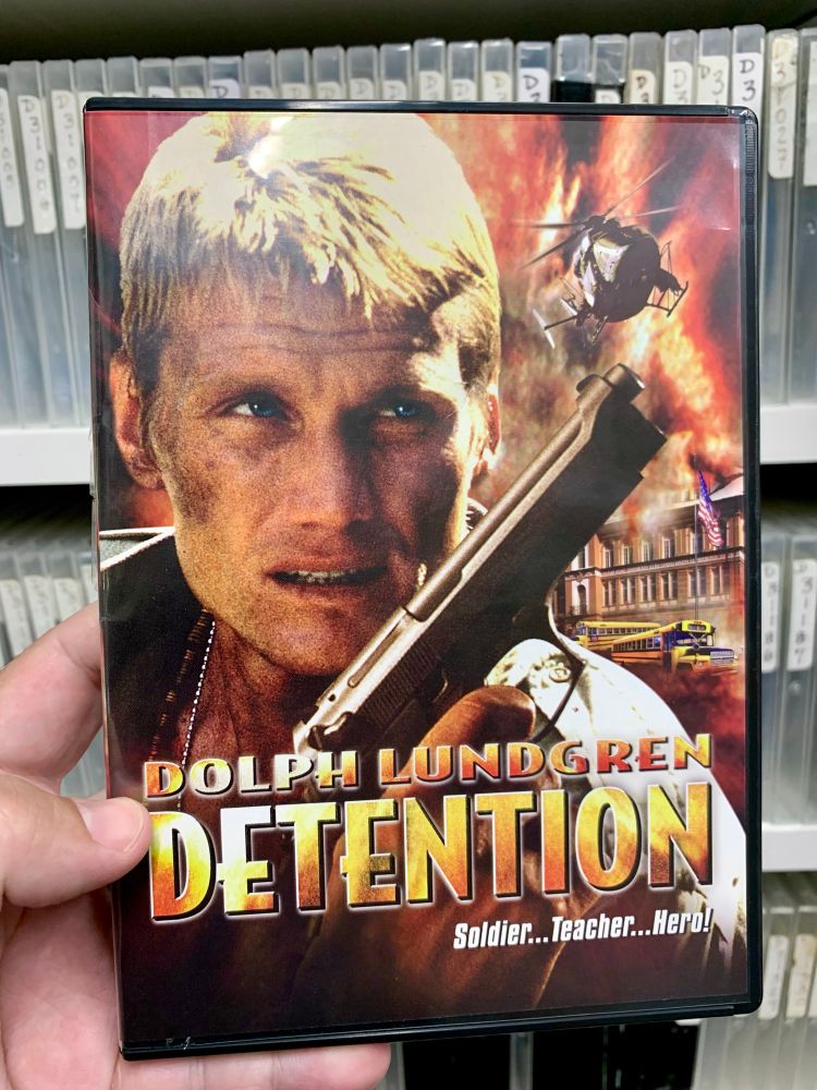 A hand holding Dolph while he’s holding a gun. A dvd cover of the 2003 movie Detention!