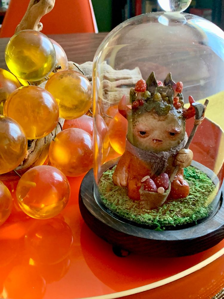 A small sculpture of a mushroom forager with a tray of glass grapes