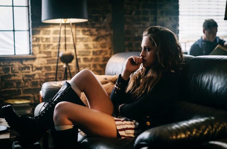 a still of darlene from mr robot lounging on a couch with her foot up. she's wearing big, knee high boots and chewing on her nail, staring off in space in anxious contemplation.