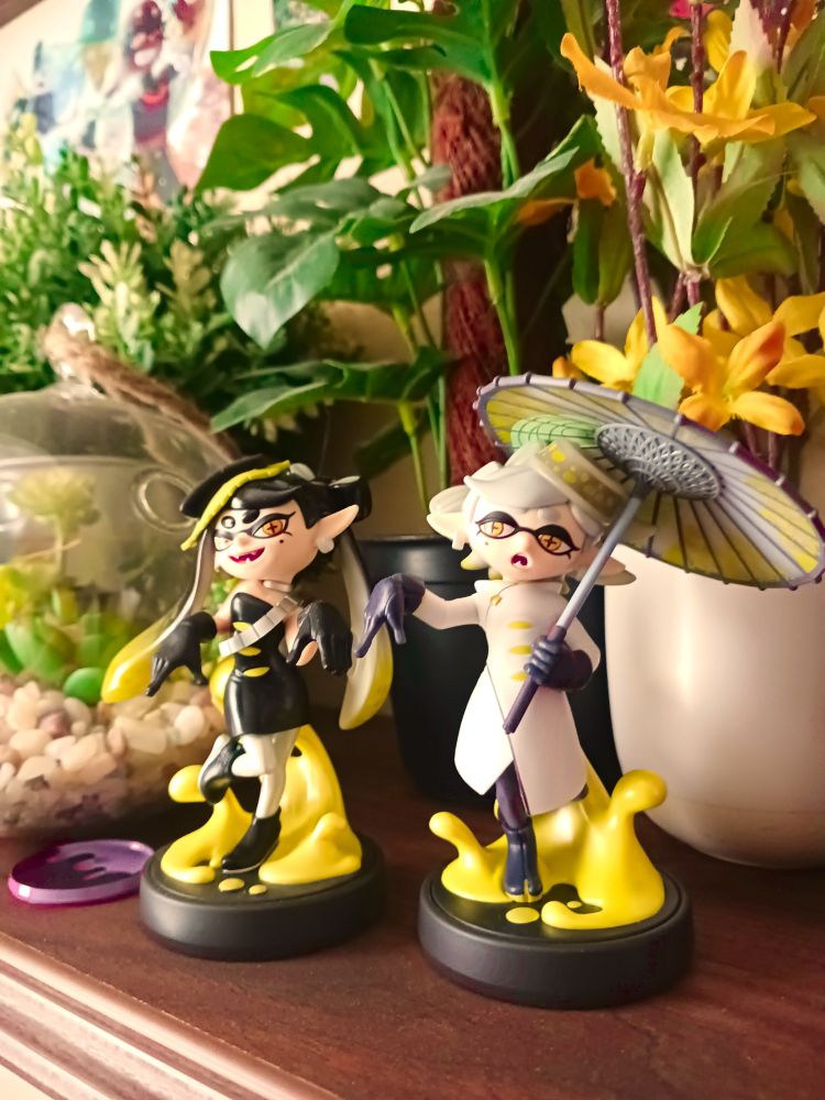 Callie and Marie Alterna Amiibo ztandinv infront of fake plants on a shelf 
