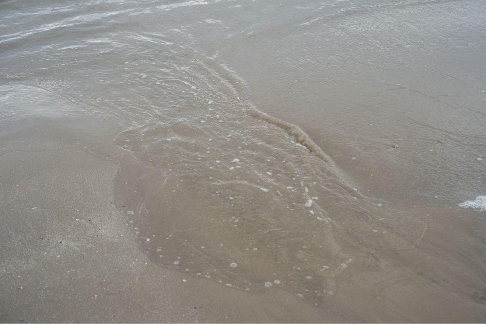 寄せてきた波が砂浜で溜まっている写真