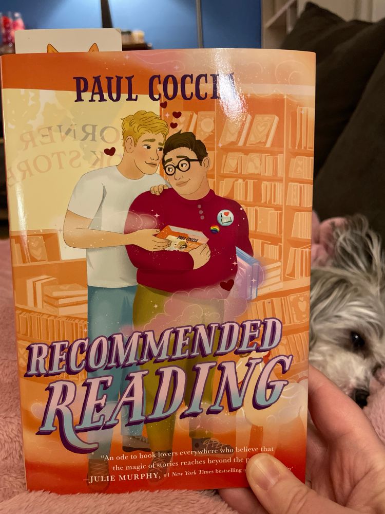 Cover of Recommended Reading by Paul Coccia. Illustration shows two young men standing close to one another in a bookstore with small hearts above their heads. 