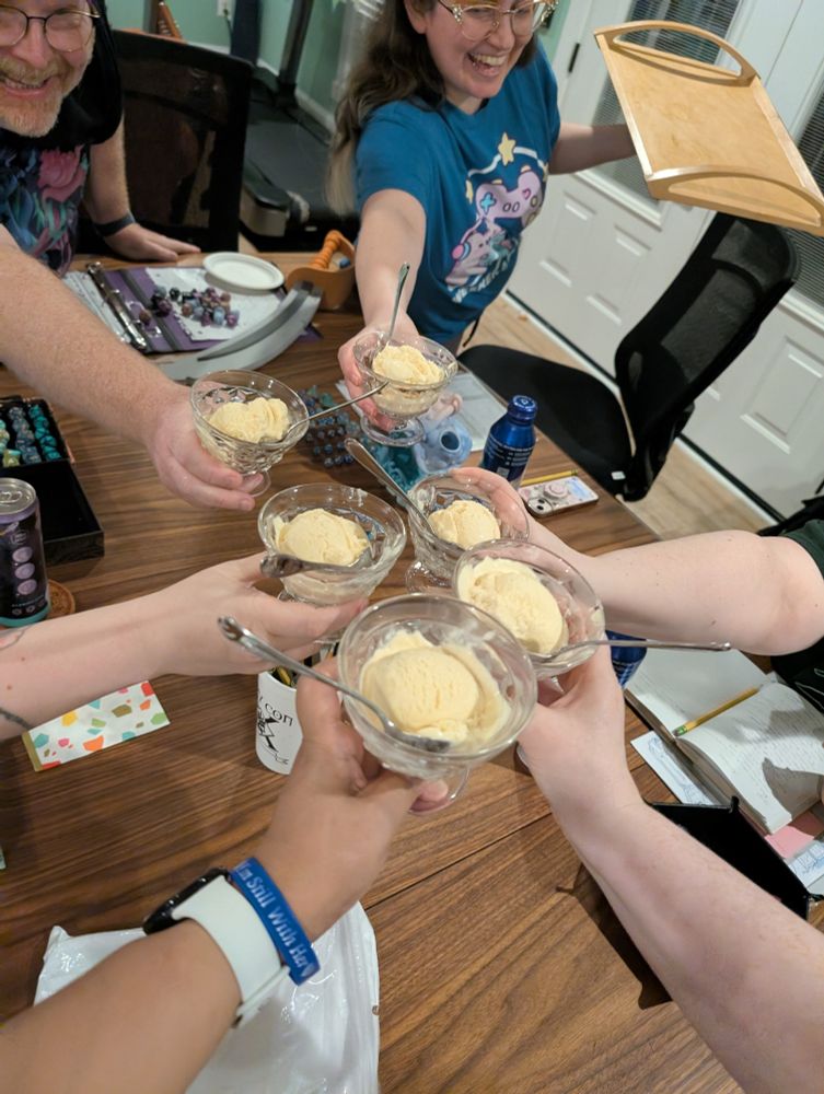 Six people toast their ice cream coupes over a D&D gaming table.