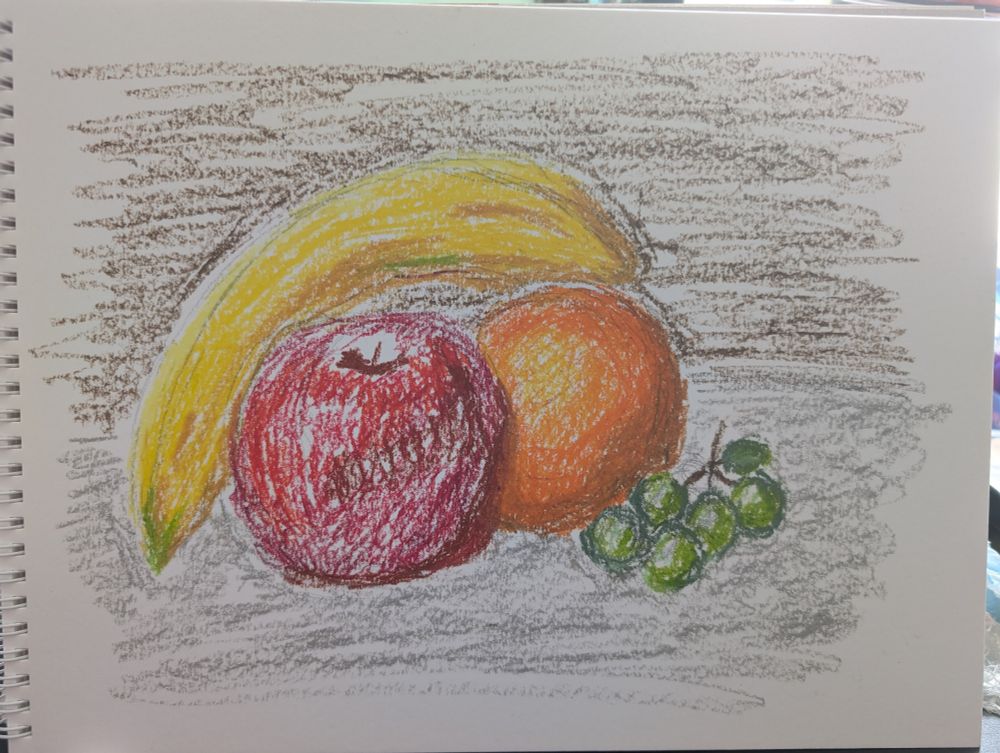 Preliminary blocking with Holbein oil pastels of a still life featuring a yellow banana, red apple, orange, and green grapes, on a grey table with a dark brown background.