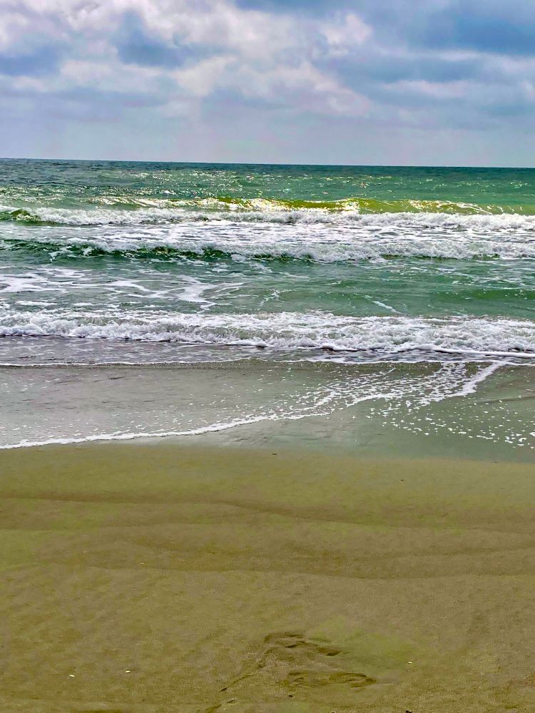 Greenish surf rolling to a sandy shore with Lacey white foam