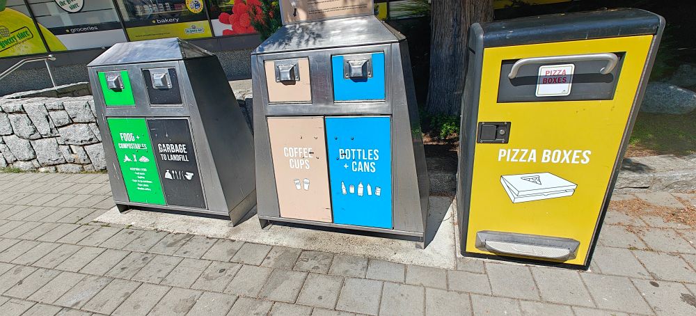 Recycling bins in Whistler, Canada. Green color is for food and compostables. Black/grey is for garbage. Tan is for coffee cups. Blue is for bottles and cans. Yellow/mustard is for pizza boxes. The latch mechanism is unlocked by sliding four fingers up under the cover, making it not something a bear could unlock.