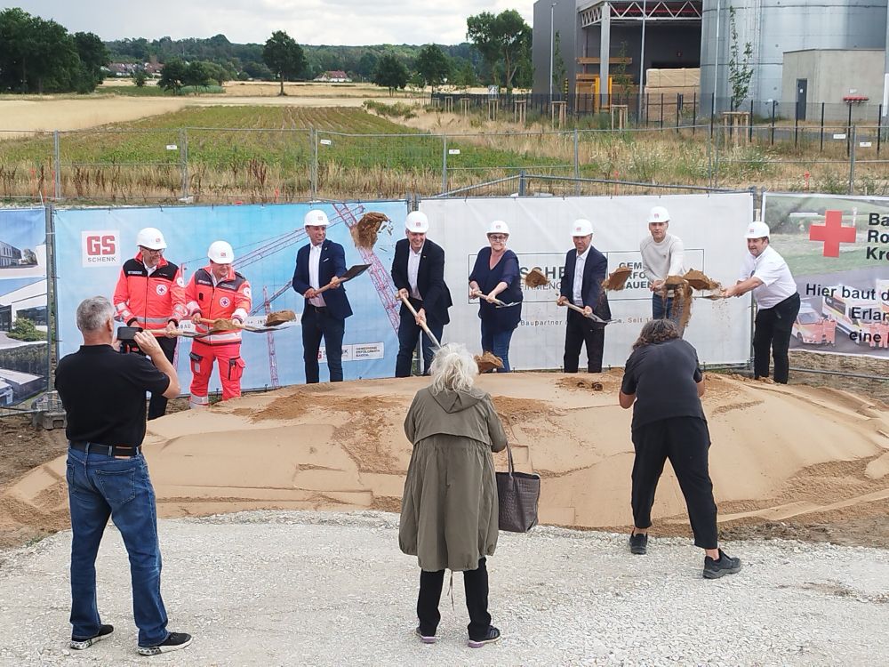 Bürgermeisterin, Landrat und Vertreter des BRK beim Spatenstich. Das Bild entstand, als der Sand auf den Spaten gerade in die Luft geworfen wurde. Im Vordergrund sind Vertreter der lokalen Presse und fotografieren den Vorgang