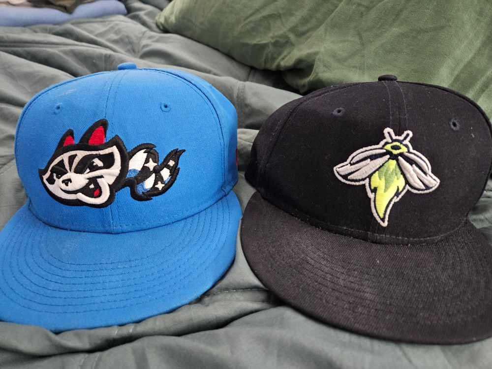 A royal blue Rocket City Trash Pandas hat and a navy blue Columbia Fireflies hat