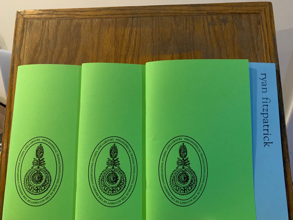 Three copies of the chapbook festshrift of my work. Yellow cover with an official looking academic-style logo and my name off to the side.