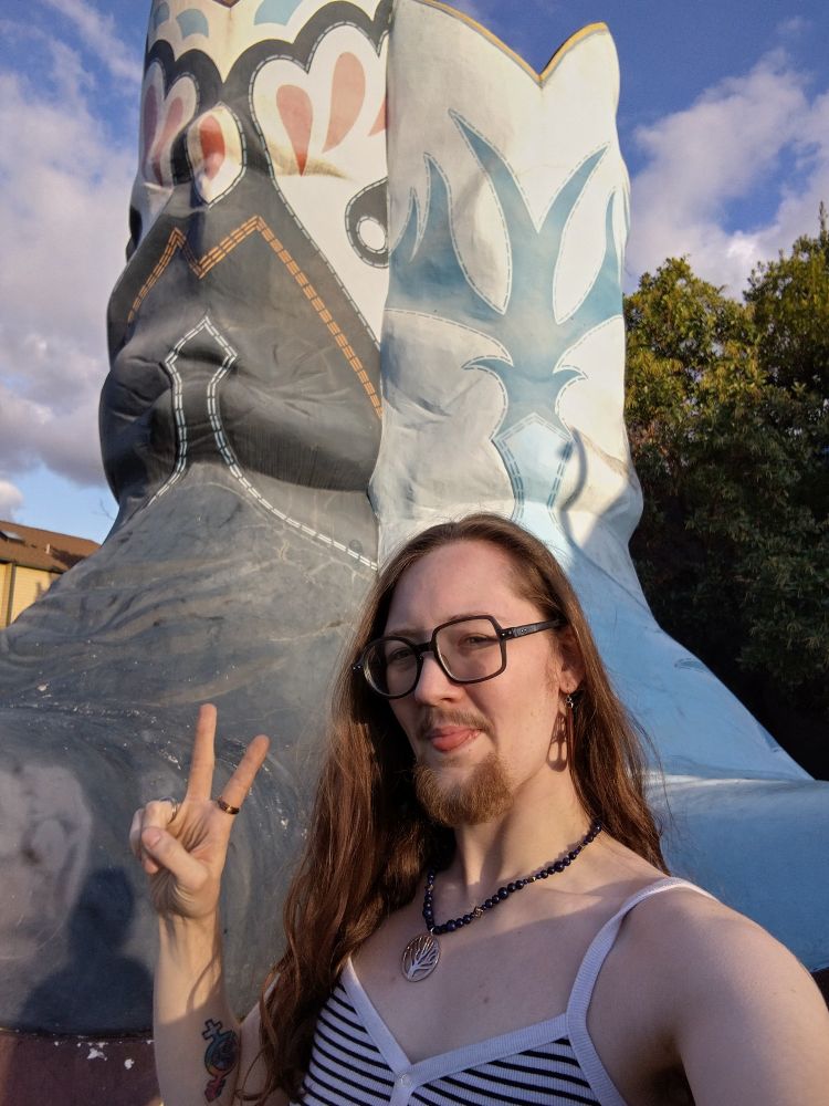 Me, sticking my tongue out and giving the peace sign in front of the large cowboy boots 