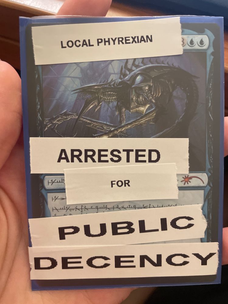 A Magic: the Gathering card-- Jin-Gitaxias, Core Augur. It's been vandalized with a labelmaker saying "Local Phyrexian arrested for public decency"