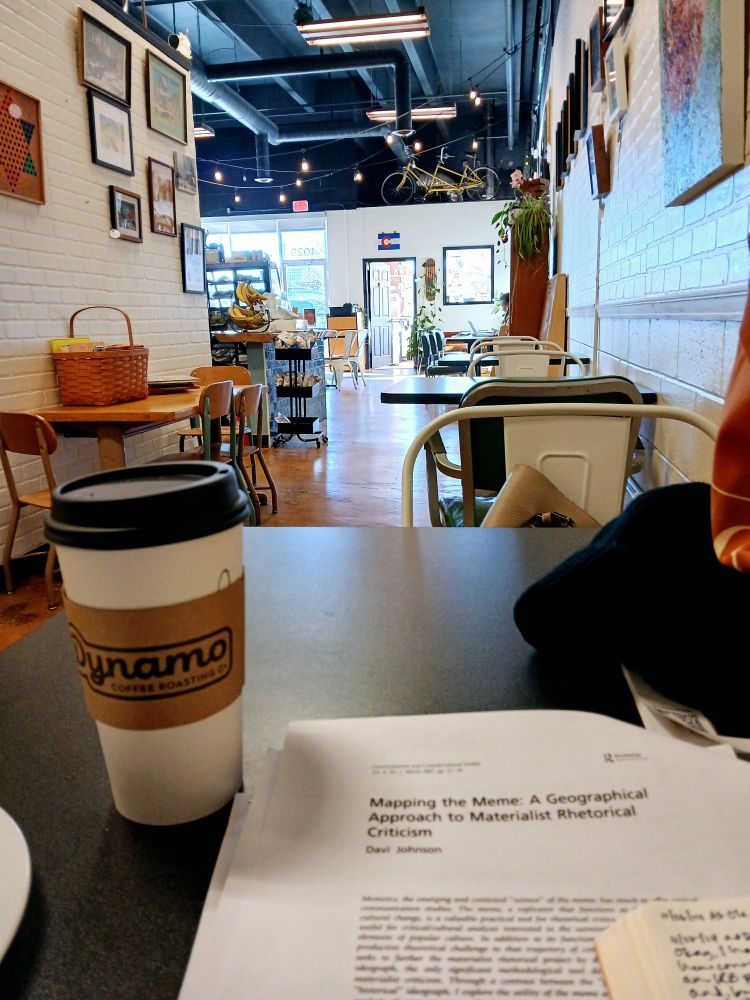 Paper coffee cup sits next to a printed article with a view of an empty coffee shop.