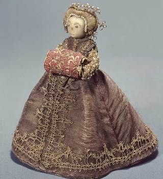 1590s cloth doll, dressed as a fashionable court lady with embroidered face, blonde hair pulled back into a pearl-decorated style, and a silk dress and large hand muff trimmed with metal lace. Collection of the Royal Armoury, Stockholm