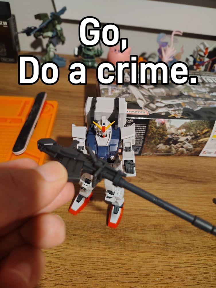 A 1:144 scale RX79 Ground Type Gunpla model, being handed a howitzer, captioned "Go, Do a crime."