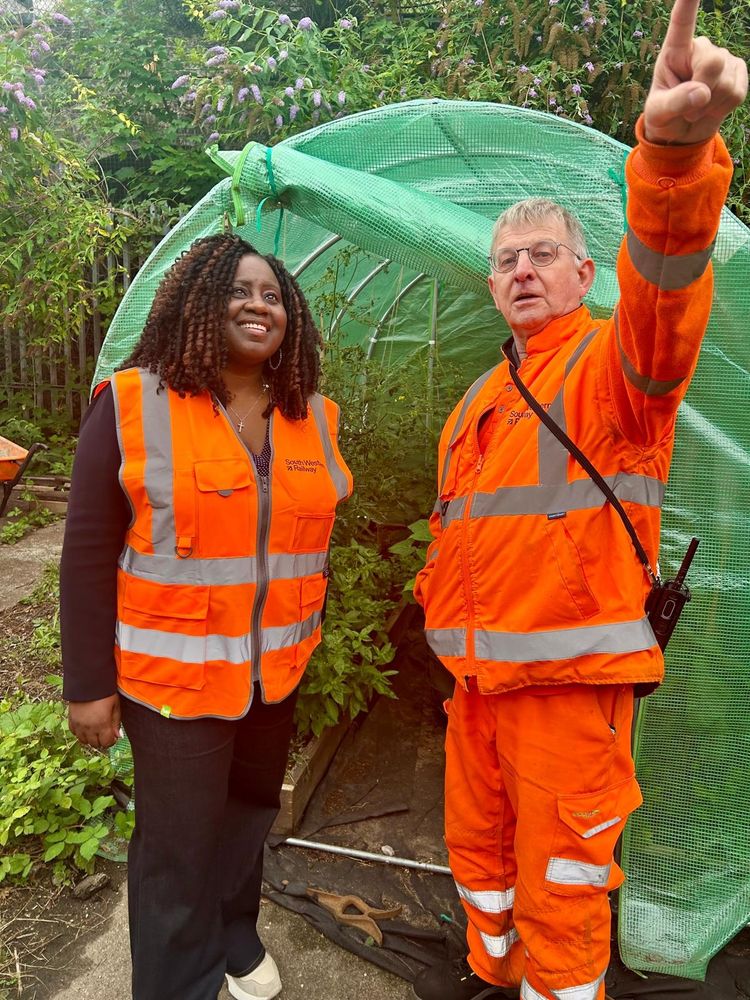 Marsha with a member of staff in the garden. Surrounded by greenery and both wearing orange high vis. Same in all photos 
