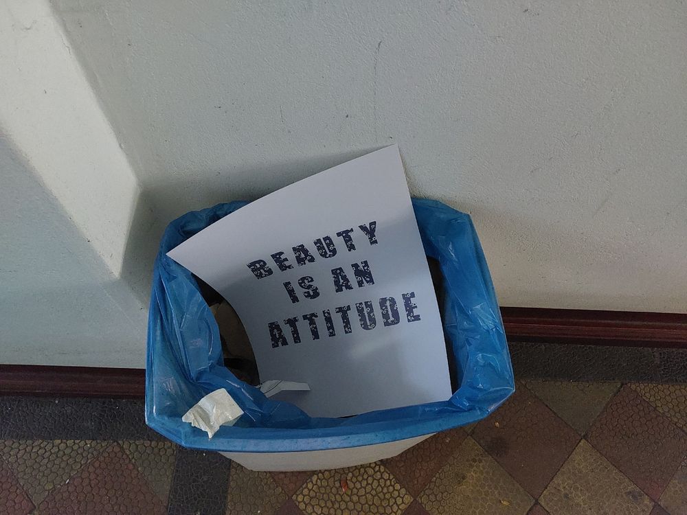 Ein Plakat mit der Aufschrift "Beauty is an attitude" liegt in einem Papierkorb