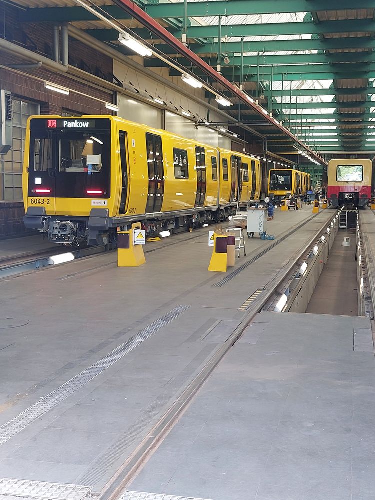 Zwei U-Bahn-Züge stehen auf dem linken Gleis, ein S-Bahn-Zug auf dem rechten Gleis. Alles in einer großen Halle.