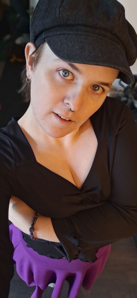 selfie of Alice in a black hat, black top, and purple skirt taken from above. fae is looking up at you and its cleavage is awesome