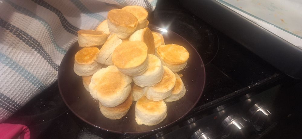 a plate of freshly baked biscuits resting on a stovetop. the brown crusts are lit up by the overhead light