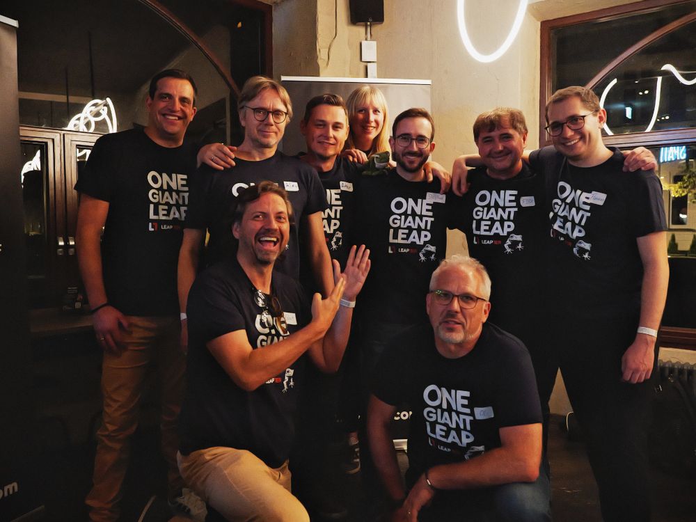 A group photo of the Leapter team at the WeAreDevelopers event. Nine team members are smiling and wearing matching black t-shirts that read “ONE GIANT LEAP”. They are gathered indoors in a warmly lit room, with a mix of standing and crouching poses, clearly celebrating together.