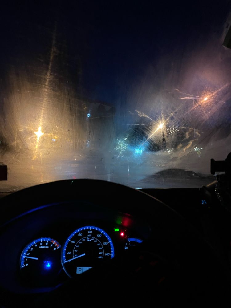 the inside of a car at night. the dashboard is lit up and the windshield is fogged up